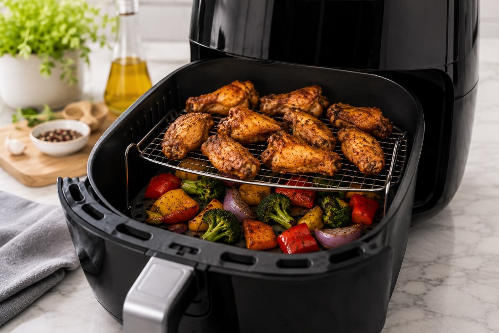 Two-level air fryer rack with chicken wings and roasted vegetables